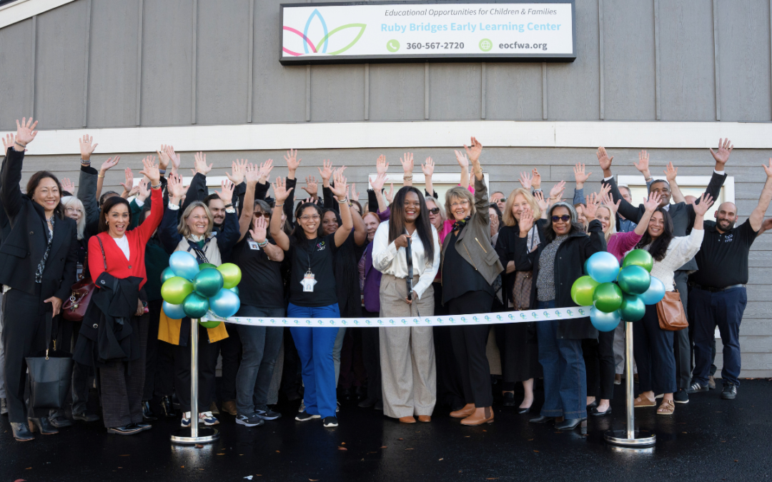 A group of staff members and supporters stand together, watching as the CEO cuts the ribbon at the grand opening of the new learning center. The scene captures a moment of excitement and celebration, with the CEO holding a large pair of scissors and the ribbon held by two stands on either side. The crowd is smiling and applauding in support of the new educational facility.